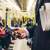 Un homme transportant un journal consulte un téléphone intelligent dans le métro.