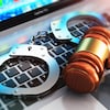 Sur un clavier d'ordinateur reposent des menottes ainsi qu'un maillet représentant la justice. 
