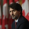 Le premier ministre Justin Trudeau assis devant des drapeaux canadiens durant une conférence de presse.