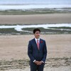 Justin Trudeau portant un coquelicot et prenant une pose solennelle sur la plage, tandis qu'on voit de l'eau et des vagues à l'arrière.