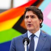 Justin Trudeau sa harap ng mikropono at sa background niya lumilipad ang Pride flag.