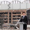 Justin Trudeau devant un lutrin. On voit derrière lui un aéroport en ruines.