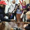 Un homme portant une casquette rouge montre son téléphone au président donald trump, assis derrière le bureau ovale, à la maison-Blanche. 