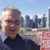 Kevin J. Johnston pose devant la ville de Calgary, une pancarte électorale à la main.