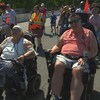 Des personnes circulent à pied et en fauteuil roulant sur une piste de course automobile. 
