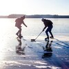 Deux personnes jouent au hockey sur un immense lac gelé. 