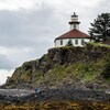 Le phare Eldred Rock en contre-plongée avec le récif et une personne qui marche sur la plage, en Alaska, juillet 2022.