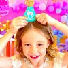 Une fillette enfile un biscuit en forme de chapeau de fête sur sa tête, devant un décor très coloré. 