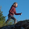 Photographie de Simone, qui marche avec des bâtons de randonnée sur un cap rocheux et montagneux.