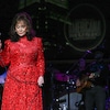 Loretta Lynn porte une robe rouge et tient un micro sur une scène. 