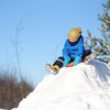 Un enfant au sommet d'un monticule de neige sur sa luge.