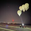 Des ballons blancs gigantesques sont lancés à l'aube depuis une piste d'aéroport.