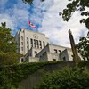La mairie de Vancouver avec son horloge, des arbres, et un drapeau canadien sur son toit.