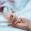 Une personne tient la main d'un malade dans un lit d'hôpital.