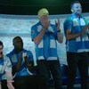 Cinq personnes portant des chandails et des foulards au couleurs de Manchester City regardent un match de soccer diffusé à l'aide d'un projecteur.