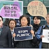 Un militant s'adresse à la foule avec un micro à côté d'autres, debout, qui brandissent des pancartes sur lesquelles on peut lire « Stop! Plastic » et d'autres messages en coréen.