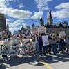 Des centaines de personnes manifestent, à Ottawa, pancarte à la main. 