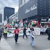 Les manifestants marchent dans la rue derrière une grande banderole qui porte la mention, en anglais : « 76 ans d'occupation, 76 ans de résistance ».