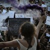 Une femme tient une bombe fumigène à bout de bras alors que devant elle des centaines de personnes, dont une bonne partie tenant des pancartes.
