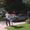 Un homme est en train de planter un panneau sur lequel est écrit À vendre dans une pelouse, devant une maison.