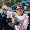 Martine Pombert tient dans ses mains une vignette de stationnement numérotée, assise dans son véhicule avec la portière côté conducteur entrouverte. 