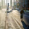 À droite, un cycliste dans la rue. À gauche, son reflet dans une fenêtre.