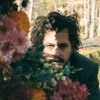 On voit le chanteur avec des fleurs, regardant la caméra.