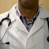 Un médecin vêtu de son sarrau, avec un stétoscope lui tombant sur les épaules. 