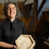 Une femme souriante tient une brique octogonale de construction. 