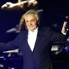Le chanteur ouvre les bras sur scène avec un micro dans la main droite. 