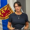 Michelle Thompson assise en conférence de presse devant un drapeau de la Nouvelle-Écosse.