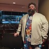  Mickaël Bergeron se tient droit dans une salle de spectacle. Sa main est posée sur une  chaise. 