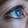 Une femme se tient devant un écran d'ordinateur alors que le logo du réseau social Facebook se réflète dans son œil. 