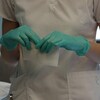 Les mains d'une infirmière, avec des gants verts, qui tient de la gaze