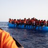 Des dizaines de migrants portant des gilets de sauvetage entassés dans un zodiac attendent d'être secourus au large de la Libye.