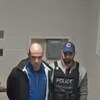 Un homme menotté et escorté par deux policiers.