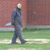 Un homme déguisé en Jason du film «Friday the 13th» marche le long d'un bâtiment. Il a un masque de hockey, une salopette grise et un faux couteau.