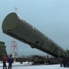 Le missile, dans un immense contenant de métal vert, est transporté à l'extérieur sur un camion remorque sous le regard de personnes vêtues de manteaux.