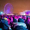 Une foule devant une scène et la roue du Vieux-Port de Montréal, à la tombée de la nuit alors qu'il neige. 