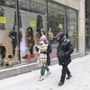 Des passants marchent au centre-ville de Montréal sous la neige, portant un couvre-visage.