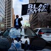 Un homme noir perché sur une voiture brandit un drapeau « Black Lives Matter ».