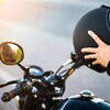 Un homme est assis sur une moto mais on voit seulement ses deux bras. Il tient un casque de moto comme s'il s'apprêtait à le mettre sur sa tête.