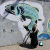 Un artiste peint un poisson sur un mur extérieur.