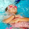Une petite fille portant des lunettes de natation est sur le dos dans une piscine.