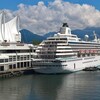 Un navire de croisière est amarré dans le port de Vancouver à côté de trois voiles de la Place du Canada et avec au loin des montagnes.
