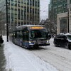 Un autobus circule sur une rue enneigée du centre-ville de Vancouver et un piéton marche sur un trottoir.