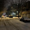 Des voitures sont stationnées le long d'une rue résidentielle. La rue et les voitures sont recouvertes de plusieurs centimètres de neige.