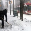 Une personne déneige le trottoir à Toronto alors qu'un tramway passe dans la rue.