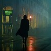 Un homme marche de dos sous la pluie dans une rue d'une grande ville.