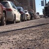 Un trottoir plein de roches longe une file de voitures stationnées.